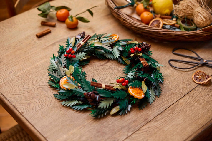 LEGO Botanical Collection 10340 Wreath laid on a wooden table beside real oranges, cinnamon and scissors